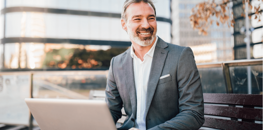 Hombre sonriendo sentado en el exterior trabajando en un computador